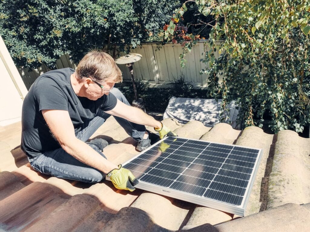 pexels-photo-9875416 A Man in Black Shirt Sitting on the Roof while Holding a Solar Panel