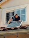 A worker installing a solar panel on a residential rooftop under bright sunlight.